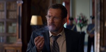 Movie still from “Murder Mystery” (2019), directed by Kyle Newacheck – A man in a suit and tie smoking a cigarette; Close Up shot, Low angle