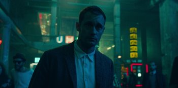 Movie still from “Mute” (2018), directed by Duncan Jones – A man in a suit standing in the dark; Medium shot, Low angle