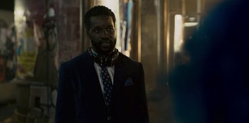 Movie still from “Mute” (2018), directed by Duncan Jones – A man in a suit and tie standing in front of a building; Close Up shot, Over the shoulder angle