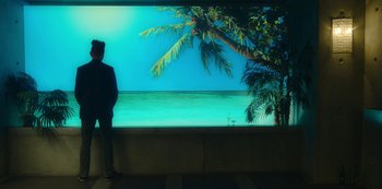 Movie still from “Mute” (2018), directed by Duncan Jones – A man standing in front of a large screen television; Wide shot, Low angle