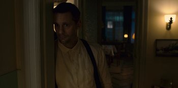 Movie still from “Mute” (2018), directed by Duncan Jones – A man standing in a dimly - lit room looking at the camera; Medium shot, Over the shoulder angle