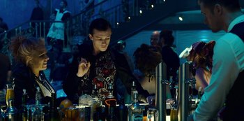 Movie still from “Mute” (2018), directed by Duncan Jones – A man standing in front of a bar filled with drinks; Medium shot, Over the shoulder angle