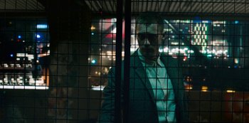 Movie still from “Mute” (2018), directed by Duncan Jones – A man in a suit standing in front of a fence; Medium shot, Low angle