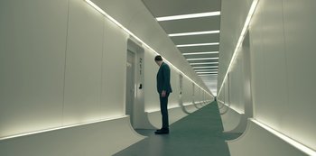 Movie still from “Mute” (2018), directed by Duncan Jones – A man in a suit standing in a hallway; Wide shot, High angle