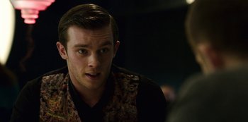 Movie still from “Mute” (2018), directed by Duncan Jones – A young man in a floral vest talking to someone in the dark; Close Up shot, Over the shoulder angle