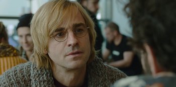 Movie still from “Mute” (2018), directed by Duncan Jones – A person wearing glasses and a sweater; Close Up shot, Over the shoulder angle