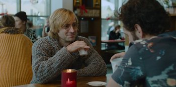 Movie still from “Mute” (2018), directed by Duncan Jones – A man sitting at a table with a woman drinking a beverage; Medium shot, Over the shoulder angle