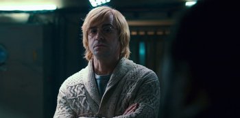 Movie still from “Mute” (2018), directed by Duncan Jones – A man with blonde hair wearing glasses and a sweater; Close Up shot, Over the shoulder angle
