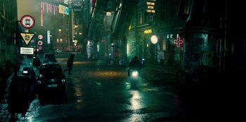 Movie still from “Mute” (2018), directed by Duncan Jones – A man riding a motorcycle down a street at night; Extreme Wide shot, High angle