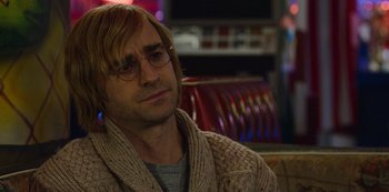 Movie still from “Mute” (2018), directed by Duncan Jones – A man sitting in front of a tv wearing a sweater; Close Up shot, Over the shoulder angle