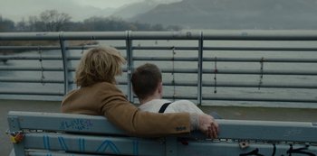 Movie still from “Mute” (2018), directed by Duncan Jones – Two people sitting on a bench near a body of water; Medium shot, Over the shoulder angle