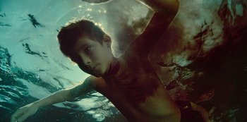 Movie still from “Mute” (2018), directed by Duncan Jones – A young man swimming in a body of water; Close Up shot, Overhead angle