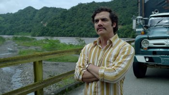 Movie still from “Narcos” (2015), created by Chris Brancato – A man standing on the side of a river; Medium shot, Low angle