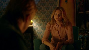 Movie still from “Narcos” (2015), created by Chris Brancato – A woman sitting in front of a man in a room; Medium shot, Over the shoulder angle