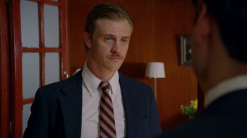 Movie still from “Narcos” (2015), created by Chris Brancato – A man wearing a suit and tie in a room; Close Up shot, Over the shoulder angle