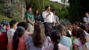 Movie still from “Narcos” (2015), created by Chris Brancato – A group of people gathered around a man in a white shirt; Wide shot, Over the shoulder angle