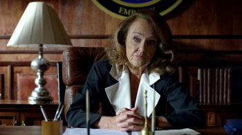 Movie still from “Narcos” (2015), created by Chris Brancato – An older woman sitting at a table in front of candles; Close Up shot, Over the shoulder angle