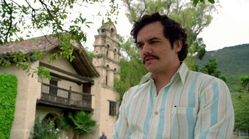 Movie still from “Narcos” (2015), created by Chris Brancato – A person wearing a striped shirt near a building; Close Up shot, Low angle