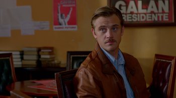 Movie still from “Narcos” (2015), created by Chris Brancato – A man sitting in a chair wearing a brown leather jacket; Close Up shot, Over the shoulder angle