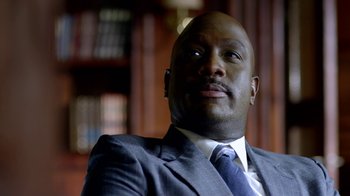 Movie still from “Narcos” (2015), created by Chris Brancato – A man in a suit and tie sitting in front of a book shelf; Close Up shot, Low angle