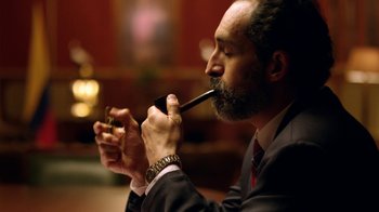 Movie still from “Narcos” (2015), created by Chris Brancato – A man in a suit holding a pipe in his mouth; Close Up shot, Low angle