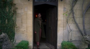 Movie still from “Men” (2022), directed by Alex Garland – A woman standing in front of an open door; Wide shot, Low angle