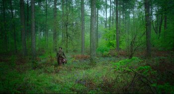 Movie still from “Men” (2022), directed by Alex Garland – A man sitting in the middle of a forest; Extreme Wide shot, High angle
