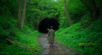 Movie still from “Men” (2022), directed by Alex Garland – A man in a trench coat standing in the woods; Extreme Wide shot, High angle