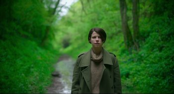 Movie still from “Men” (2022), directed by Alex Garland – A woman standing in the middle of a path in the woods; Medium shot, Low angle