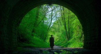 Movie still from “Men” (2022), directed by Alex Garland – A person is standing in the woods under a bridge; Extreme Wide shot, Low angle