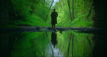 Movie still from “Men” (2022), directed by Alex Garland – A person standing in front of a body of water; Extreme Wide shot, High angle