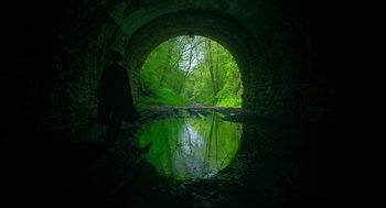 Movie still from “Men” (2022), directed by Alex Garland – A person standing in front of a river under a bridge; Extreme Wide shot, Low angle