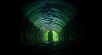 Movie still from “Men” (2022), directed by Alex Garland – A man standing in a dark tunnel with a green light coming from it; Extreme Wide shot, Low angle