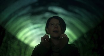 Movie still from “Men” (2022), directed by Alex Garland – A woman standing in a tunnel looking up at the sky; Medium shot, Low angle