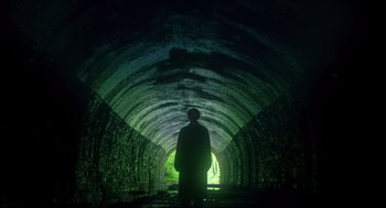 Movie still from “Men” (2022), directed by Alex Garland – A man standing in a tunnel with a light shining on it; Extreme Wide shot, Low angle