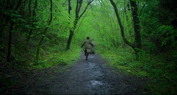 Movie still from “Men” (2022), directed by Alex Garland – A man running down a path in the woods; Extreme Wide shot, High angle