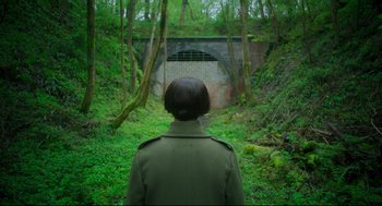 Movie still from “Men” (2022), directed by Alex Garland – A woman standing in the middle of a lush green forest; Wide shot, High angle