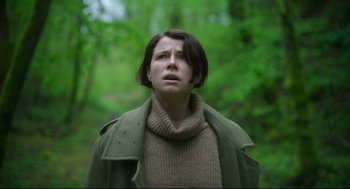 Movie still from “Men” (2022), directed by Alex Garland – A woman standing in a wooded area with her eyes wide open; Medium shot, Low angle