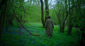 Movie still from “Men” (2022), directed by Alex Garland – A person walking through a forest with trees and flowers; Wide shot, High angle