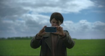 Movie still from “Men” (2022), directed by Alex Garland – A woman taking a picture with a cell phone; Medium shot, Low angle
