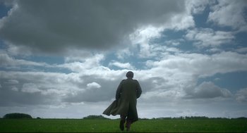 Movie still from “Men” (2022), directed by Alex Garland – A man in a long coat walking in a grassy field; Extreme Wide shot, Low angle