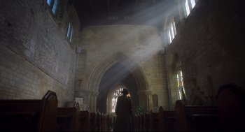 Movie still from “Men” (2022), directed by Alex Garland – A person standing inside of a church with a light coming through the window; Extreme Wide shot, Low angle