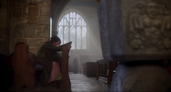 Movie still from “Men” (2022), directed by Alex Garland – A man sitting at a pew in front of a window; Wide shot, Low angle