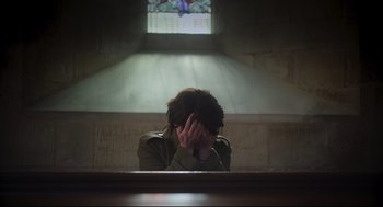 Movie still from “Men” (2022), directed by Alex Garland – A woman sitting in a church holding her head in her hands; Medium shot, Over the shoulder angle