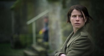Movie still from “Men” (2022), directed by Alex Garland – A woman in a green coat sitting in front of a tree; Close Up shot, Over the shoulder angle
