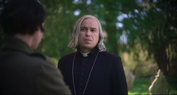 Movie still from “Men” (2022), directed by Alex Garland – A man with long blonde hair wearing a priest's outfit; Close Up shot, Over the shoulder angle