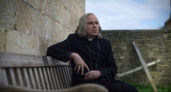 Movie still from “Men” (2022), directed by Alex Garland – A man sitting on top of a wooden bench wearing headphones; Close Up shot, Over the shoulder angle