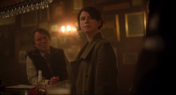 Movie still from “Men” (2022), directed by Alex Garland – A woman standing in front of a man in a suit; Medium shot, Over the shoulder angle