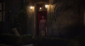 Movie still from “Men” (2022), directed by Alex Garland – A woman standing in front of a door with a white dog; Wide shot, Over the shoulder angle