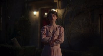 Movie still from “Men” (2022), directed by Alex Garland – A woman in a pink dress standing in front of a building; Medium shot, Low angle